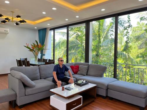 a man sitting on a couch in a living room at Friendly villa SH Đại Lải 4 phòng ngủ in Phúc Yên