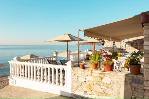 uma varanda com cadeiras e guarda-sóis e o oceano em Potokaki Beachfront Hotel em Pythagoreio
