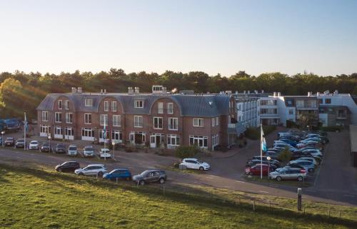 un grand bâtiment avec des voitures garées dans un parking dans l'établissement De Pelikaan Texel Appartmenten, à De Koog
