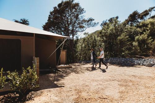 two people walking down a dirt road next to a house at Drift Off Grid Luxury Eco Glamping in Tarakohe