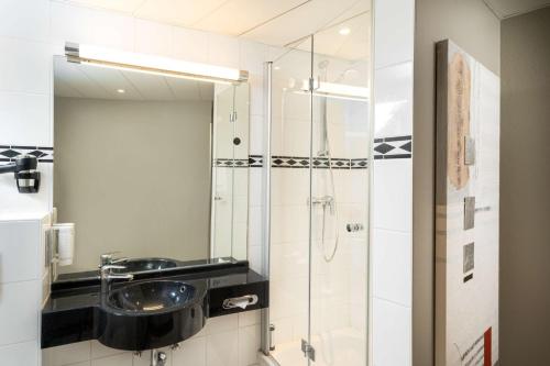 uma casa de banho com um lavatório e um chuveiro com um espelho. em elaya hotel hannover city em Hanôver