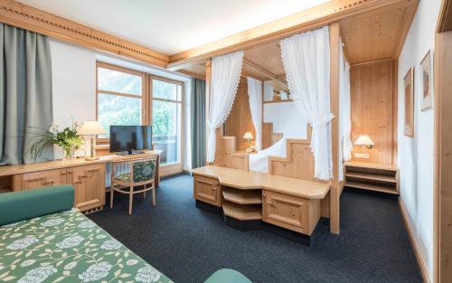 a room with a bedroom with a desk and a television at Ferien & Wellnesshotel Windschar in Brunico