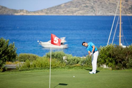 a man playing golf in front of the ocean at Porto Elounda Golf & Spa Resort, Six Senses Spa in Elounda