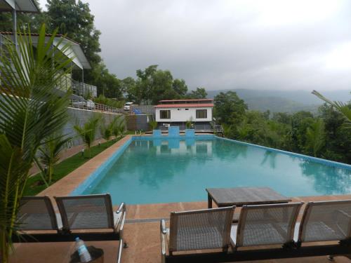 a swimming pool with chairs and a house in the background at THE NIHAL RESORT in Mahabaleshwar