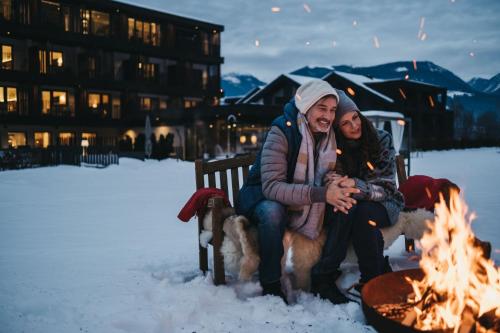 a man and woman sitting on a bench next to a fire at Hotel Rudolf in Brunico