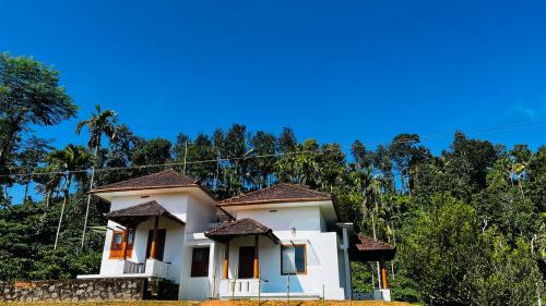 a white house with trees in the background at Pristine Hills in Meppādi