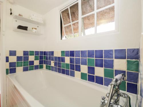 a bath tub in a bathroom with blue and green tiles at 1 Peacock Cottage in Salisbury