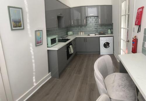 a kitchen with gray cabinets and a washer and dryer at The Princess Flat, Helensburgh. in Helensburgh