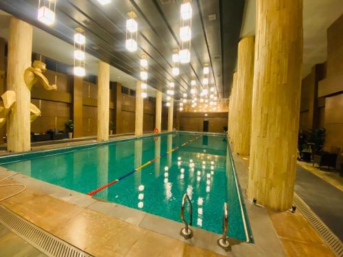 a large swimming pool in a building with columns at Holidazzle Serviced Apartments Bahria Town in Rawalpindi