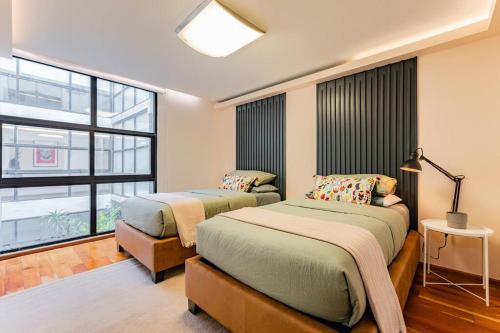 two beds in a room with a large window at Stylish apartment with private roof top & jacuzzi in Mexico City