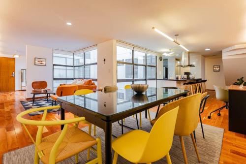 a dining room with a glass table and yellow chairs at Stylish apartment with private roof top & jacuzzi in Mexico City