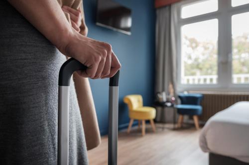 a woman is holding a suitcase in a hotel room at Hôtel du Parc Thionville Centre in Thionville