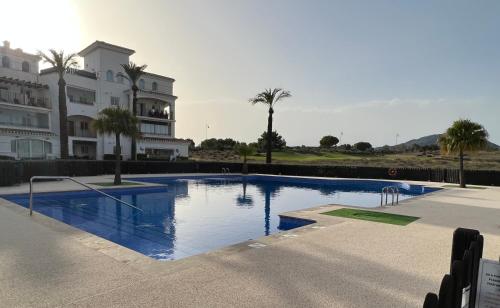 a swimming pool in front of a building with palm trees at Apartment in Hacienda Riquelme Golf Resort in Sucina