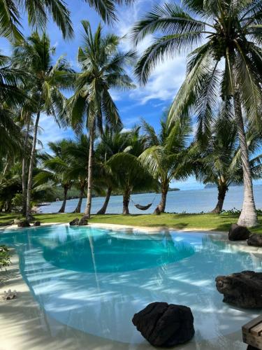 a swimming pool on a beach with palm trees at The Beach House Ocam Ocam in Busuanga