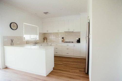 a kitchen with white cabinets and a clock on the wall at Figo Place in Benalla