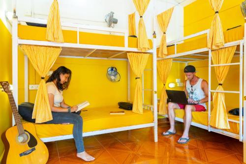 two people sitting on bunk beds in a room with a guitar at Whoopers Hostel Palolem in Palolem