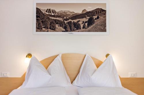 1 cama con almohadas blancas y una foto en la pared en Villa Erina App B, en Ortisei