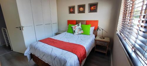 um pequeno quarto com uma cama com almofadas verdes e vermelhas em Villa in the Village em Joanesburgo