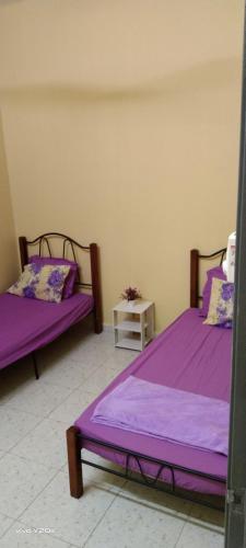 duas camas num quarto com lençóis roxos em HOMESTAY KAKMAH em Jasin