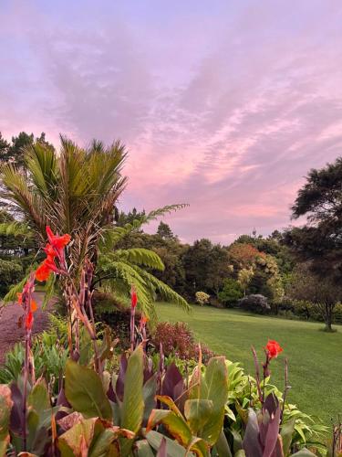 un jardín con flores rojas y un campo verde en Romantic vintage retreat away in West Auckland, en Swanson