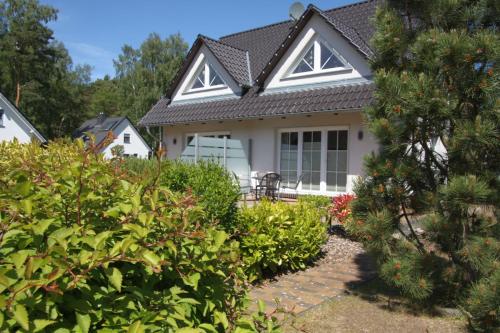 una casa blanca con techo negro y algunos arbustos en Trassenheide, Ferienidyll Neubauer, en Ostseebad Karlshagen