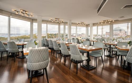 Un comedor con mesas y sillas y ventanas. en Adamar Hotel-Special Category, en Estambul