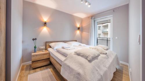 a bedroom with a bed with white sheets and a window at Apartamenty Sun & Snow Bursztynowe Osiedle Jantar in Jantar