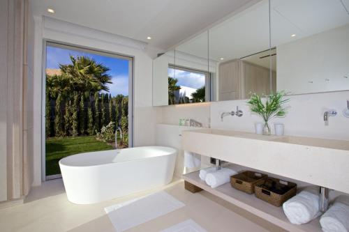 ein weißes Bad mit einer Badewanne und einem großen Fenster in der Unterkunft Contemporary Ibizan Villa Cala Conta Dream Short Walk To Beach San Jose in Cala Comte
