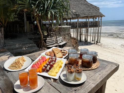 a table with plates of food and drinks on a beach at Z-Lodge Zanzibar in Kiwengwa