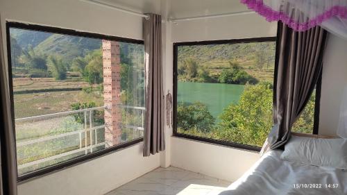 a bedroom with two large windows with a bed and a view at Riverside Homestay in Cao Bằng