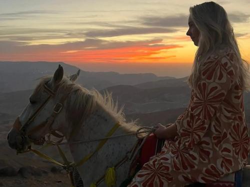 Dana Sunset Eco Camp في دانا: امرأة تقف بجانب خيل ابيض وقت الغروب