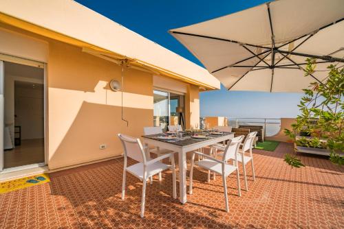 une salle à manger avec une table, des chaises et un parasol dans l'établissement Baie Roquebrune - Vue mer - Parking - AJ, à Roquebrune-Cap-Martin