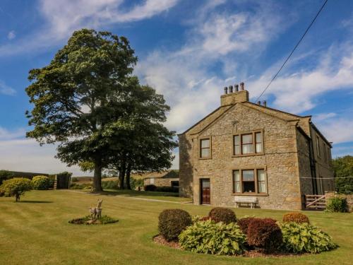 an old stone house in a field with a tree at Low Skibeden Cottage in Skipton