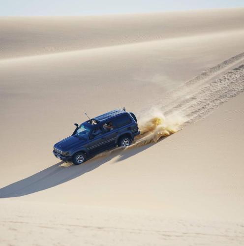 Un camión azul conduciendo a través de la arena en el desierto en Escape Camp, en Bawati