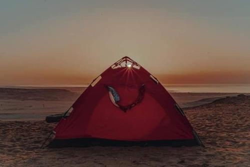 a red tent sitting on the sand on the beach at Escape Camp in Bawiti