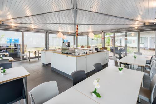 ein Restaurant mit weißen Tischen, Stühlen und Fenstern in der Unterkunft Sport Arena Hotel in Waldshut-Tiengen