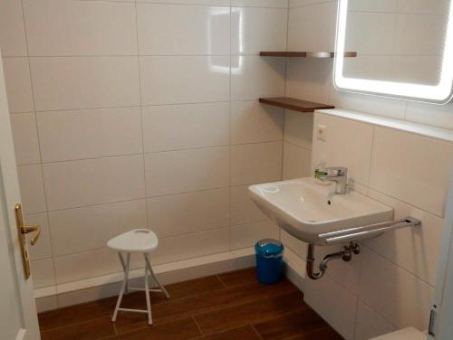 a white bathroom with a sink and a stool at Appartement Fördetraum am Strand von Wassersleben App 9 in Harrislee