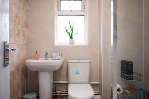 a bathroom with a toilet and a sink and a window at Cozy 3-Bedroom Home in Luton in Luton