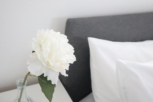 una flor blanca en un jarrón sobre una mesa junto a una cama en Twelve Thirty Serviced Apartments - Balham, en Londres