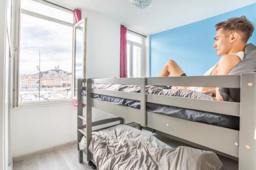 a man sitting on a bunk bed in a room with a window at Hostel Ambassade Bretonne Vieux-Port in Marseille