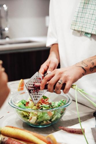 a person adding seasoning to a salad in a bowl at Level Los Angeles - Downtown South Olive in Los Angeles