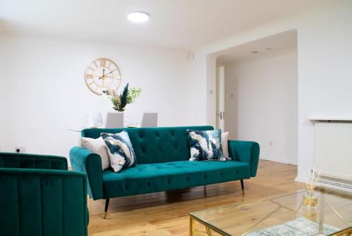 a living room with a green couch and a clock at DELUXE Tranquil Central 2 Bedroom Home-Free Parking, WIFI, Garden Views, University of Birmingham, Botanical Gardens, Edgbaston cricket in Birmingham