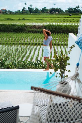 a woman standing in a field next to a pool at Woywoy Escape Samu (Adults Only) in Ubud