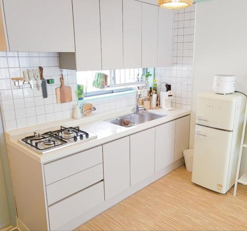 eine Küche mit weißen Schränken, einer Spüle und einem Kühlschrank in der Unterkunft Eeumgil in Daegu