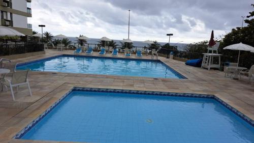 a large blue swimming pool with chairs and a building at Apartamento com toda infra e em frente a praia in Rio de Janeiro