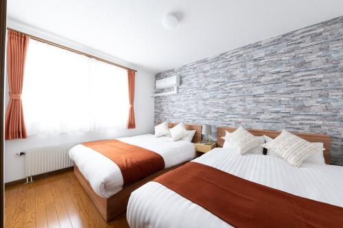 a bedroom with two beds and a brick wall at HONGO 11 HOTEL in Tsukisappu