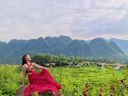 a woman in a red dress sitting on a rock in a field at Inh La Home Pu Luong in Pu Luong