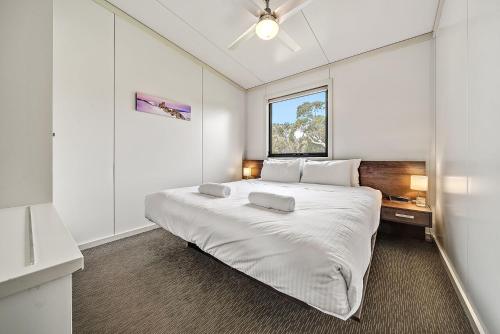 a white bedroom with a large bed with a window at Ecocrackenback 4 Sustainable chalet close to the slopes in Crackenback