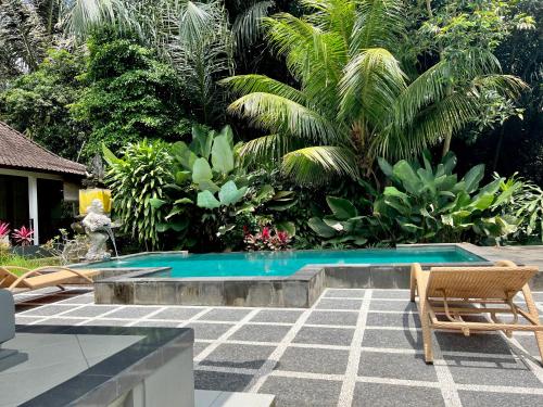 basen w ogrodzie z dwoma krzesłami i drzewami w obiekcie Manuaba Inn w mieście Ubud