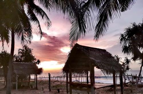 a sunset on the beach with a hut and palm trees at Helios Beach Resort in Tangalle